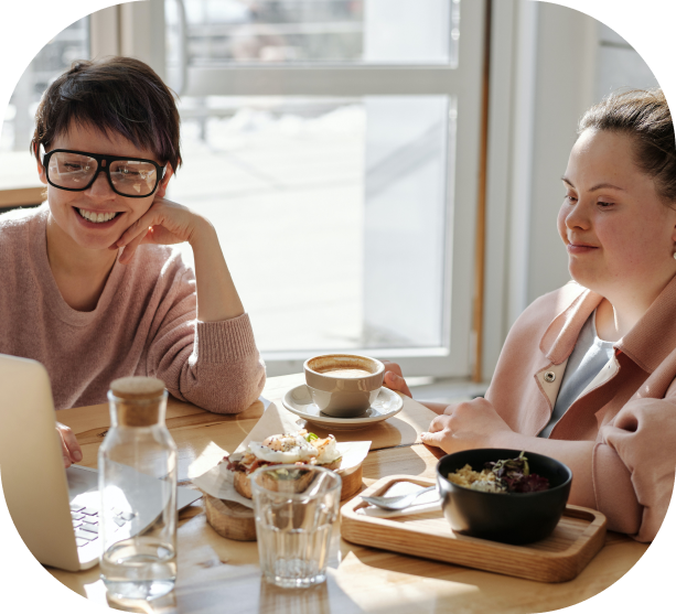 A person with Down syndrome smiling while having breakfast with a friend.